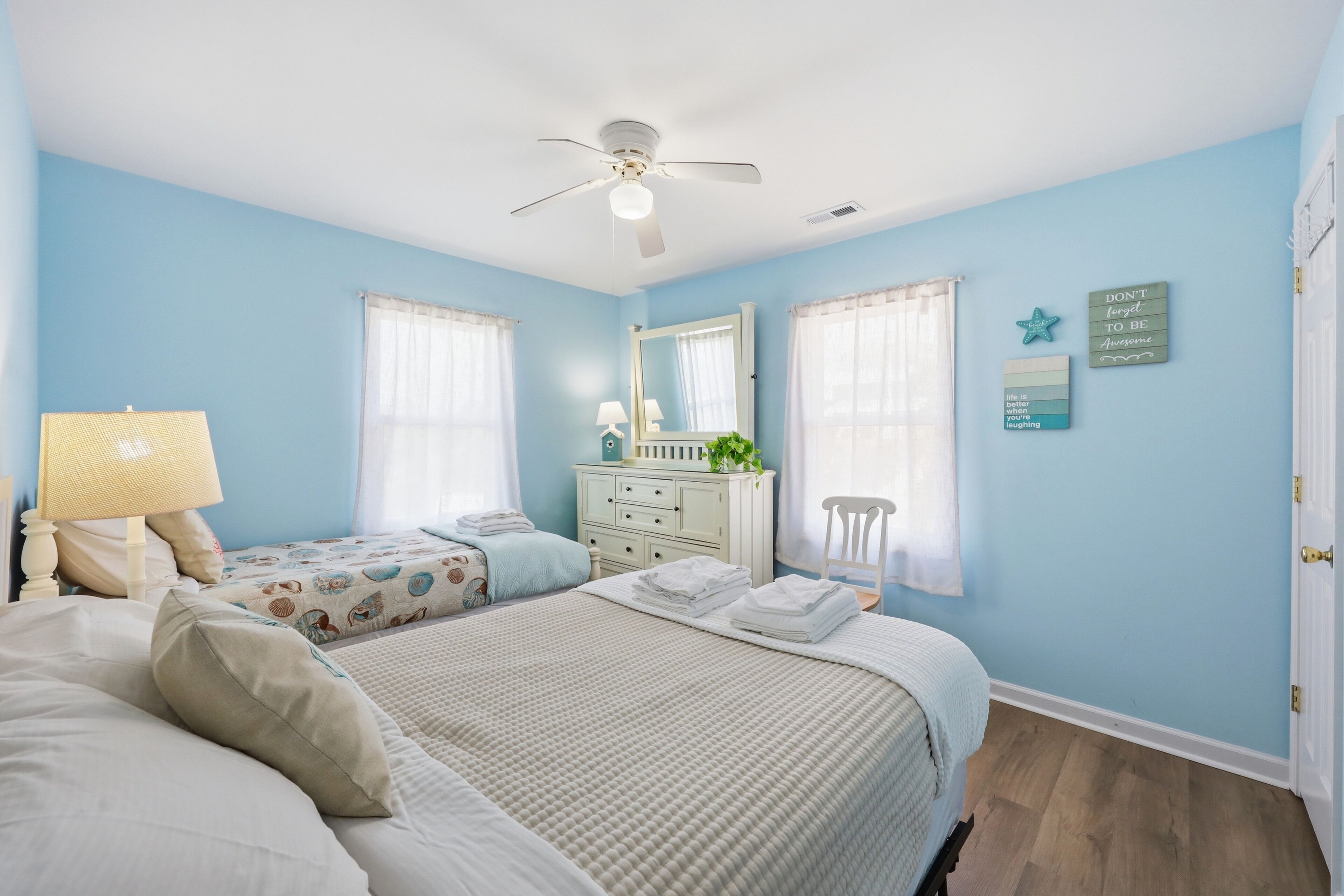 A bedroom with two beds, a ceiling fan, a dresser, a chair, and a window with curtains.