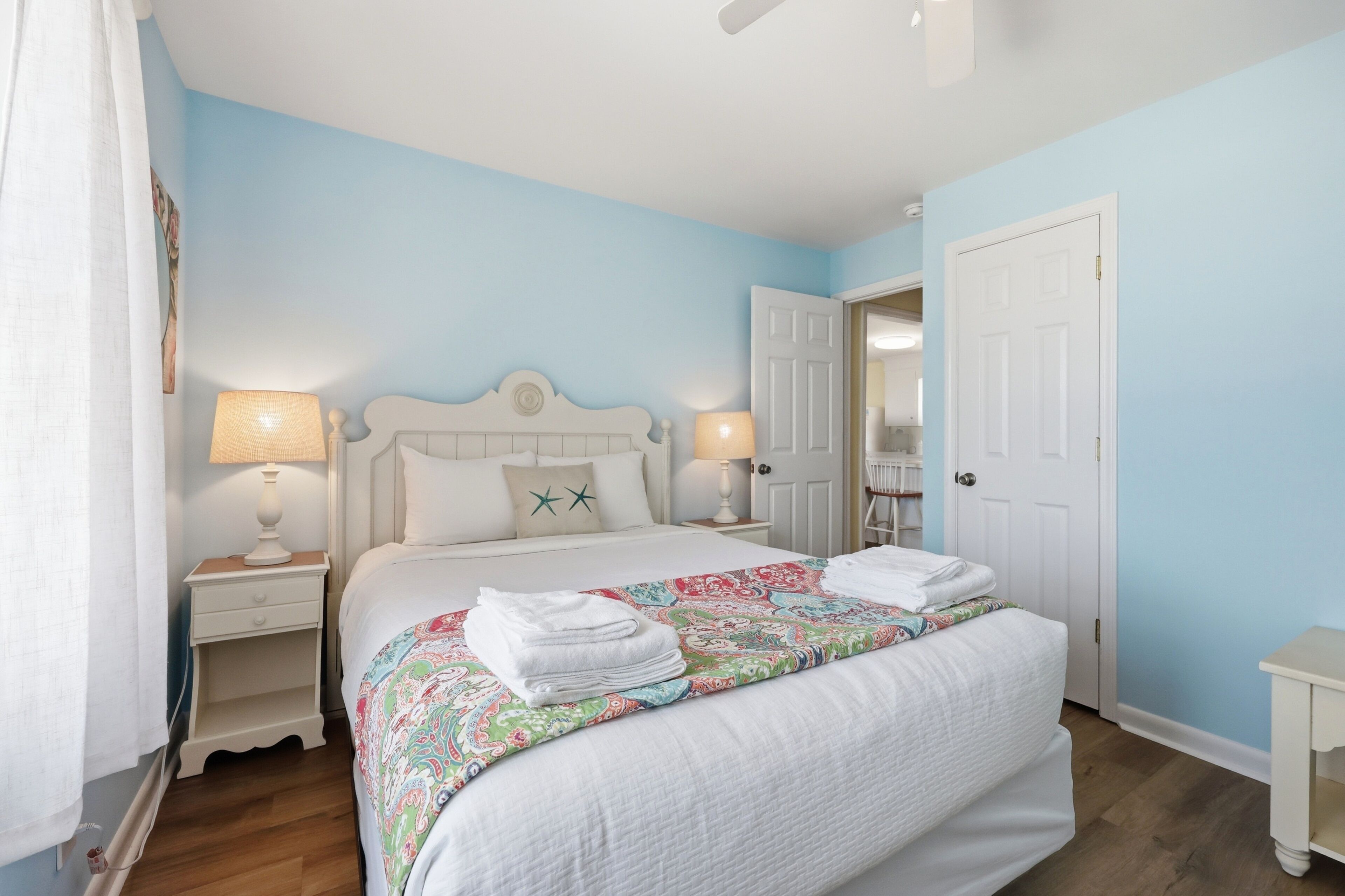 A bedroom with a bed, two bedside tables with lamps, a door, and a mirror.