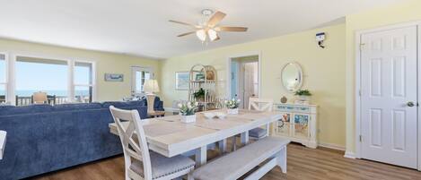 Un espace repas comprenant une table, des chaises, un banc, un ventilateur de plafond et une vue sur l’extérieur.