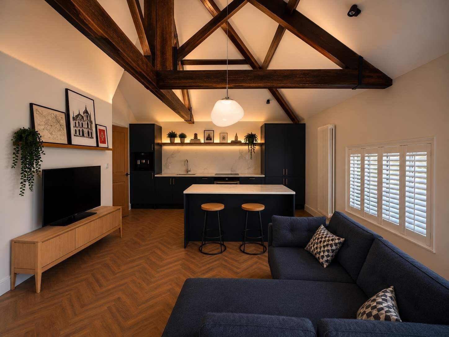 A modern kitchen with a central island, wooden beams, a TV, and a sofa with a patterned pillow.