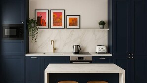 A modern kitchen with dark blue cabinets, a marble countertop, and a wooden ceiling. There are three framed pictures on the wall, a coffee maker, and two stools. - The Bridge - Penthouse Apartment (York)