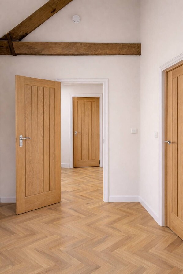 A hallway with wooden doors and herringbone-patterned flooring. - The Bridge - Penthouse Apartment (York)