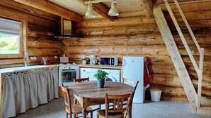 A cozy log cabin kitchen with wooden walls, a dining table with chairs, a stove, microwave, refrigerator, and a washing machine.
