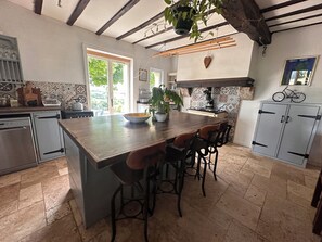 Une cuisine avec un îlot central, des tabourets de bar, une cuisinière et un vélo posé sur le dessus d’une armoire.