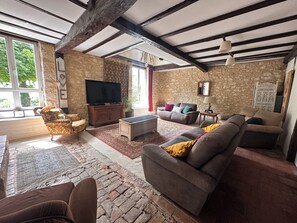 Un salon avec des murs en pierre, un plafond en bois, un téléviseur et un canapé.