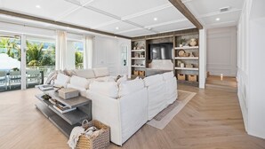 Een ruime woonkamer met een witte bank, houten vloeren en een grote televisie.