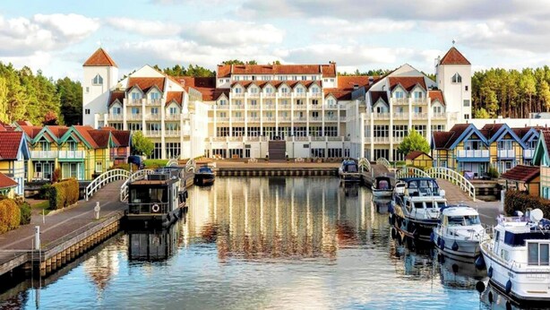 A canal-side hotel with multiple buildings, boats docked along the water, and a bridge connecting the buildings. - Sunday Resort Hafendorf Disability Access (Rheinsberg)