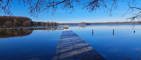 A wooden pier extending into calm water with a forested shoreline in the background.