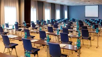 A conference room with rows of tables and chairs, water bottles on each table, and a projector screen on the wall.