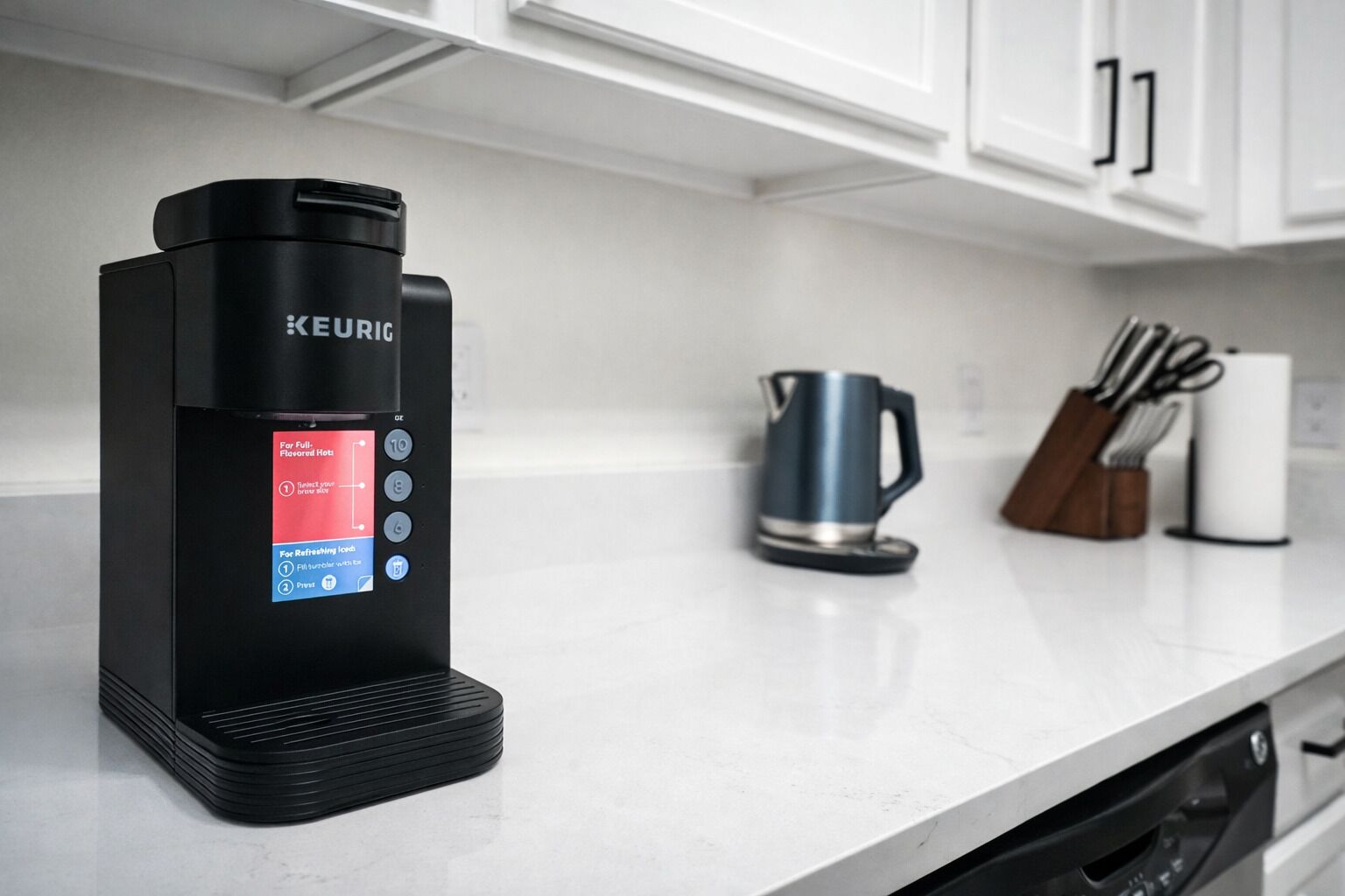 A Keurig coffee machine on a kitchen counter with a kettle and utensils in the background.