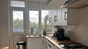 Una cuina moderna amb armaris blancs, fogó de gas, cafetera i un rentaplat.