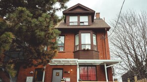 A two-story brick house with a gabled roof, a bay window on the second floor, and a covered front porch. - 0ne bed with shared   bathroom (Toronto)