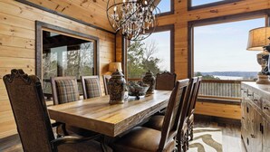 A wooden dining room with a large table, chairs, and a chandelier. There are large windows offering a view of the outdoors. - Epic Mountain Views: Hot Tub, Games and Firepit (Ellijay)