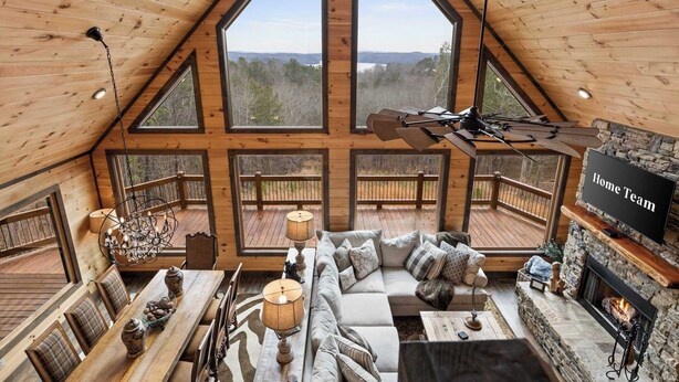 A cozy cabin interior with a large wooden ceiling, a stone fireplace, a comfortable sofa, and a television. - Epic Mountain Views: Hot Tub, Games and Firepit (Ellijay)