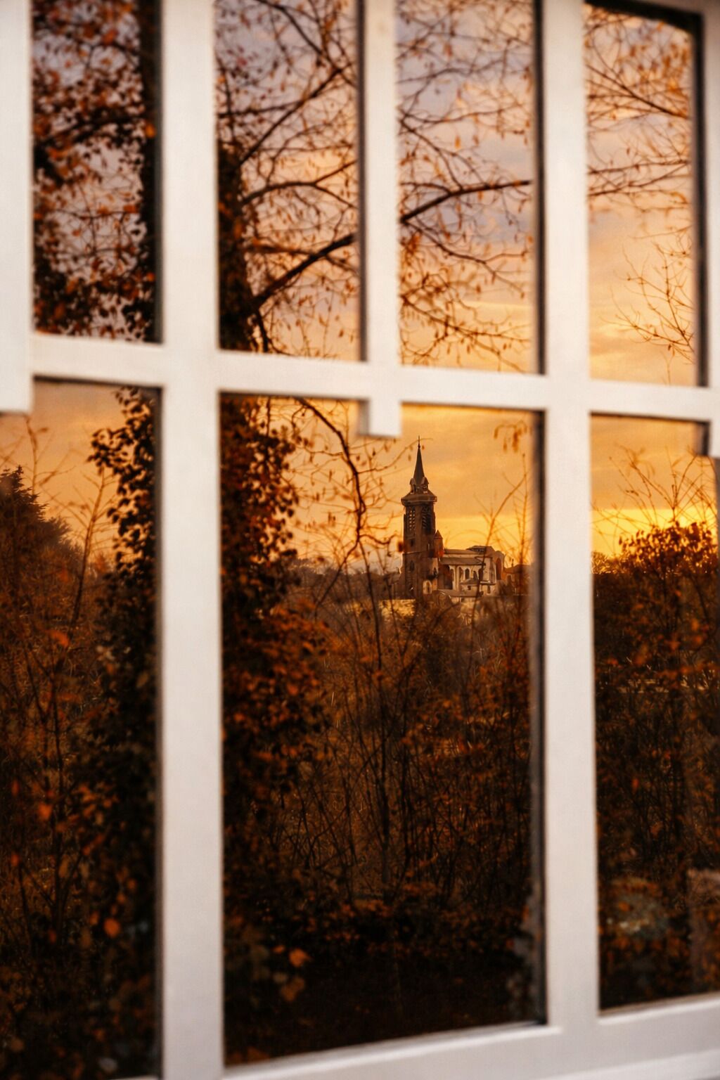 A view through a window with a church visible in the background, surrounded by trees.