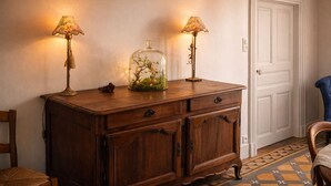 Un mueble de madera con dos lámparas, una campana de cristal con plantas y una puerta blanca al fondo.