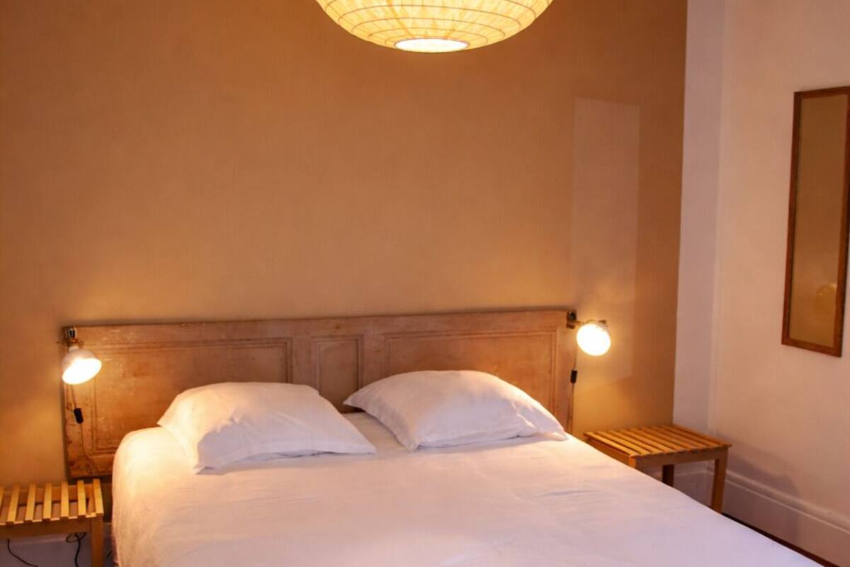 Un lit bien fait, avec une tête de lit en bois, deux tables de chevet avec des lampes et un luminaire suspendu.