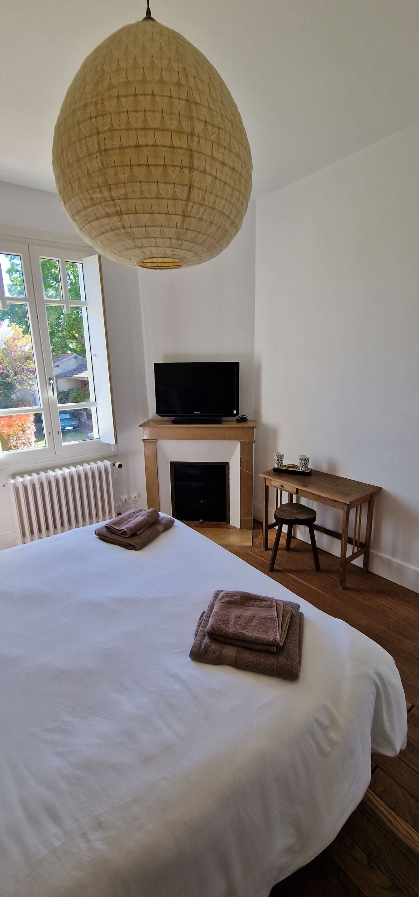 Een slaapkamer met een groot bed, een televisie op een standaard, een houten bureau en een hanglamp.