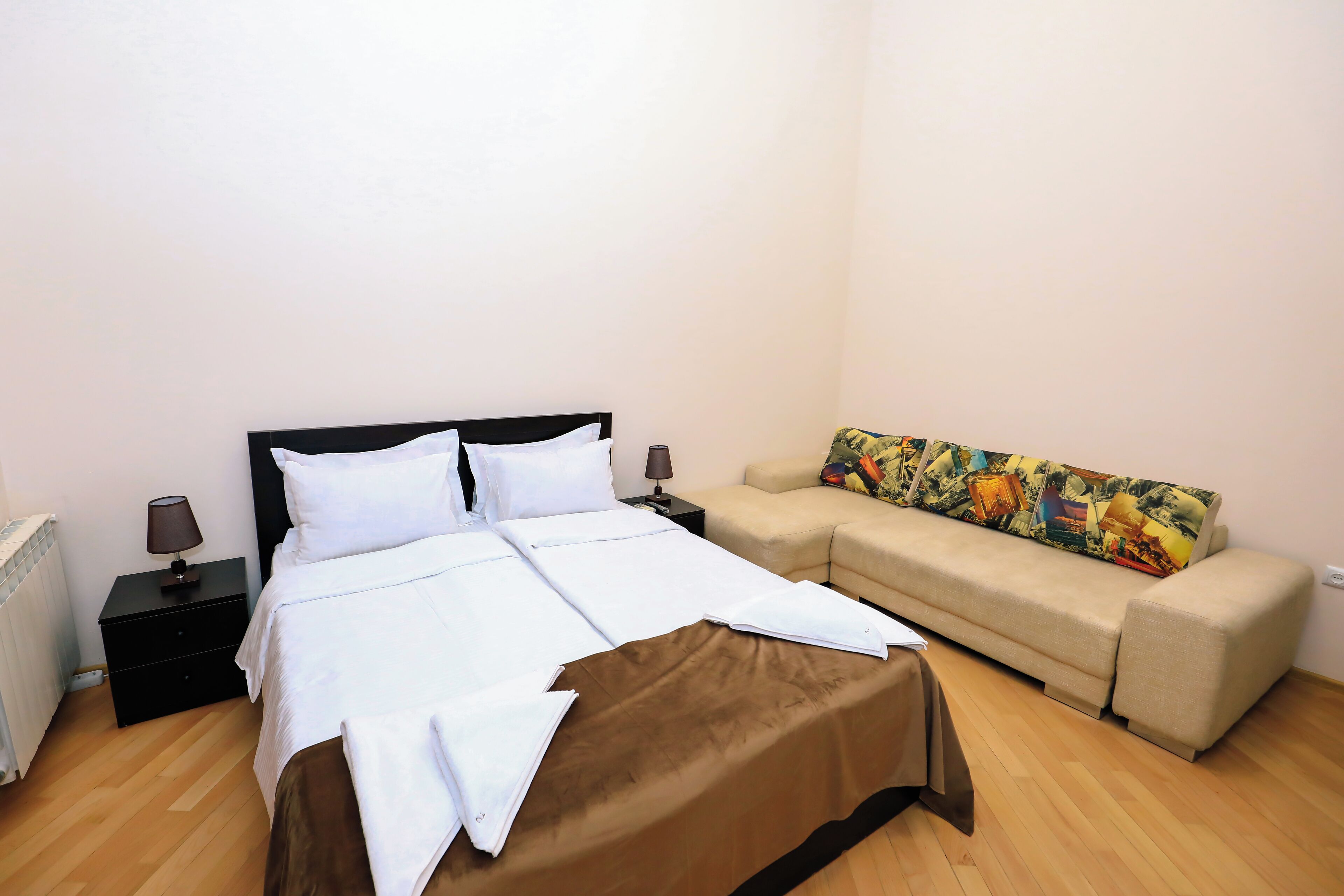 A bedroom with a bed, a nightstand, a lamp, a sofa, and a colorful cushion.
