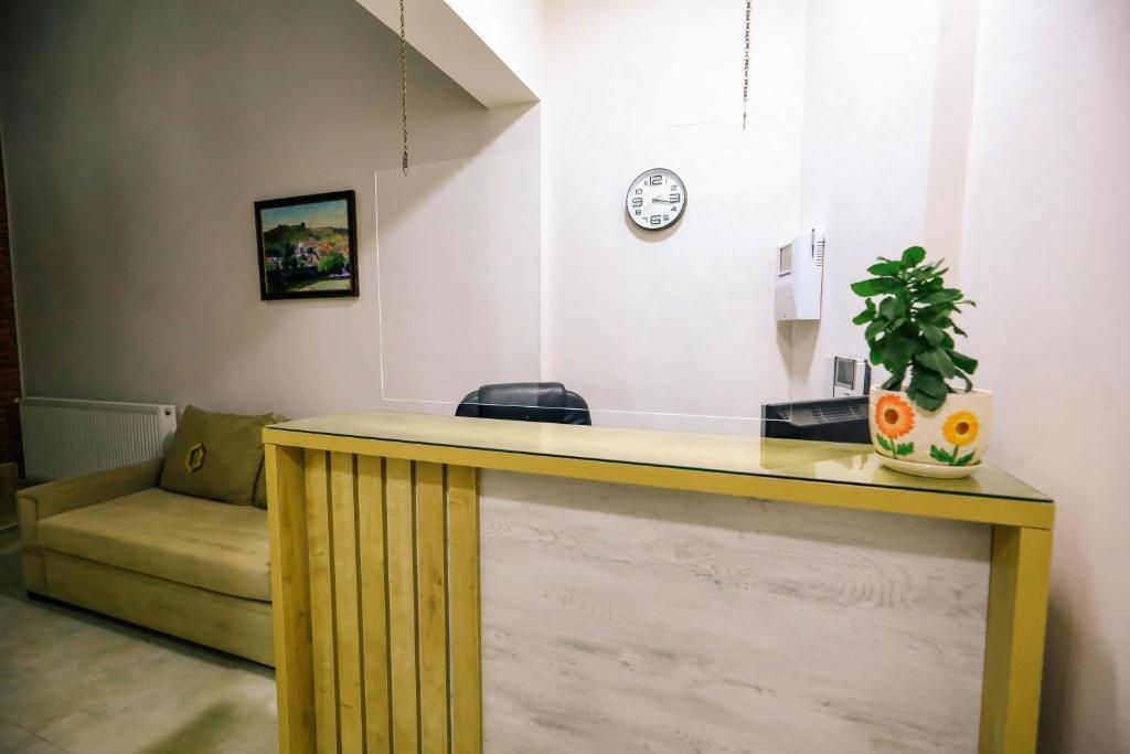 Un área de recepción con un escritorio de madera, un sofá, un reloj, un radiador y una planta.