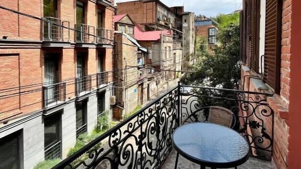 A balcony with a wrought iron railing, a round table, and a wicker chair. - Tamarisi Old Tbilisi (Tbilisi)