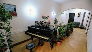 A grand piano in a well-lit room with wooden flooring, surrounded by potted plants, a painting on the wall, and a door in the background. - Tamarisi Old Tbilisi (Tbilisi)