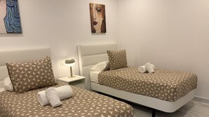 Two beds with geometric patterned bedding, a bedside table with a lamp, and artwork on the walls. - Sunning 2 bedrooom apartment 5 minutes walk to seafront. (Tías)