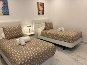 Dos camas con ropa de cama de diseño geométrico, una mesita de noche con una lámpara y cuadros en las paredes.