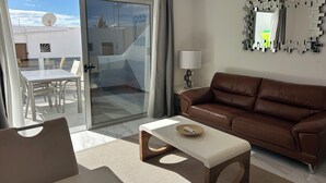 A modern living room with a brown leather sofa, a white coffee table, and a glass door leading to a balcony. - Sunning 2 bedrooom apartment 5 minutes walk to seafront. (Tías)
