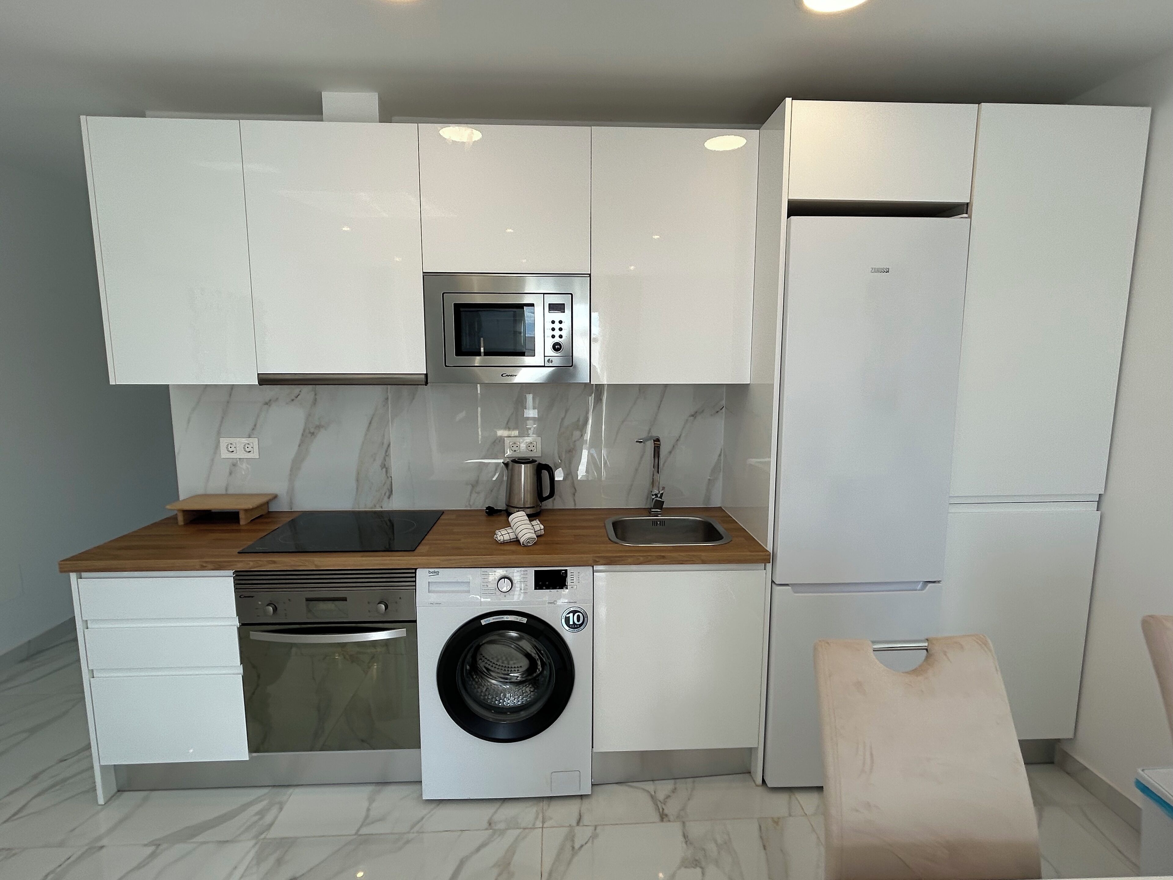 Una cocina compacta con armarios blancos, microondas, lavavajillas, lavadora y refrigerador.