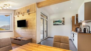 A modern kitchen with a built-in stove, a flat-screen TV mounted on a wooden wall, and a dining area with a wooden table and chairs.