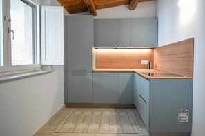 Eine kompakte Küche mit grauen Schränken, einer Holz Arbeitsplatte und einem Fenster mit Aussicht.