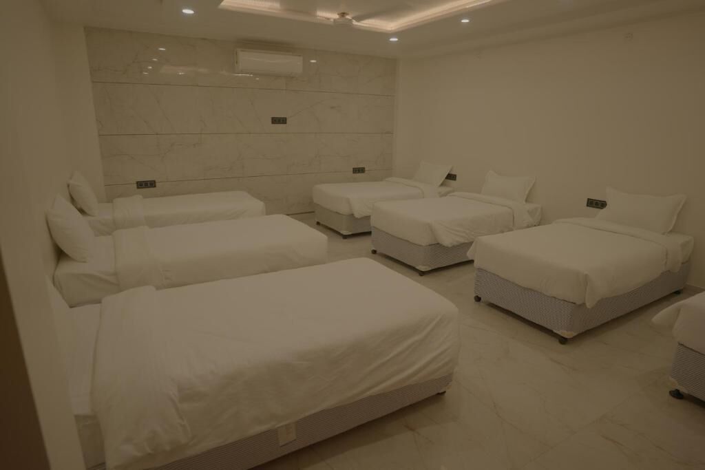Ein Hotelzimmer mit vier nebeneinander stehenden Betten, einer Marmorwand und einer Decke mit eingelassenen Leuchten.