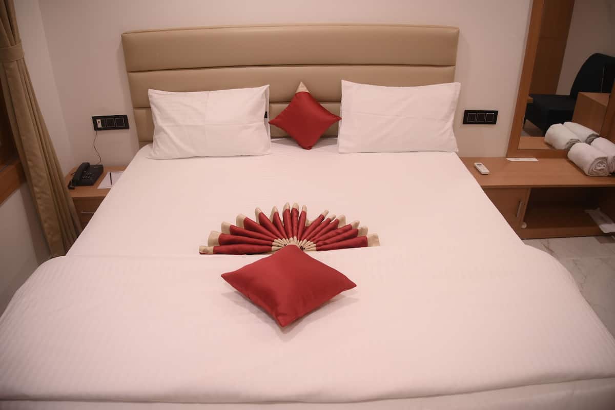 Un lit bien fait, agrémenté d’oreillers blancs et rouges, d’un coussin décoratif rouge et d’une composition en forme d’éventail composée de coussins rouges et beige.