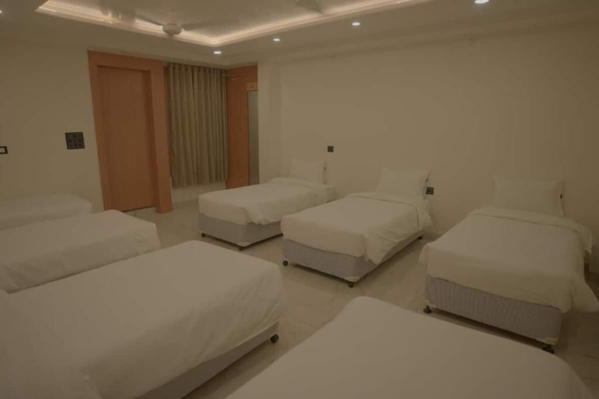Une chambre d’hôtel avec quatre lits simples, une porte donnant sur une salle de bain et un ventilateur de plafond.