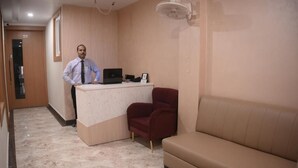 Un área de recepción con un escritorio, una computadora portátil, una silla roja y un sofá color crema.