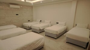 Habitación de hotel con cuatro camas individuales, piso de baldosas de mármol y una pared blanca con unidad de aire acondicionado.