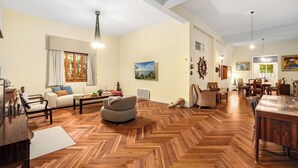 A spacious living room with a herringbone wood floor, a sofa, a coffee table, and a dining area with chairs and a table. - Historic & Modern Home with Garden (Haifa)