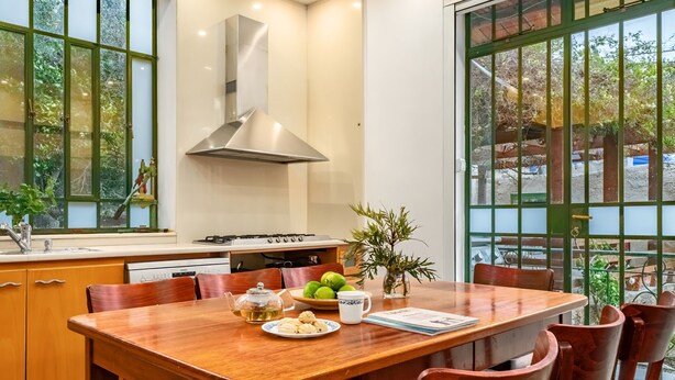 A dining area with a wooden table, chairs, a stove, and a window with a view of greenery. - Historic & Modern Home with Garden (Haifa)