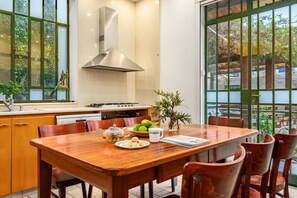 A dining area with a wooden table, chairs, a stove, and a window with a view of greenery. - Historic & Modern Home with Garden (Haifa)