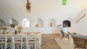 A dining area with white chairs and a table set for a meal, a hanging light fixture, and a rustic ceiling. - Masseria Mammella with pool and by the beaches (Puglia)