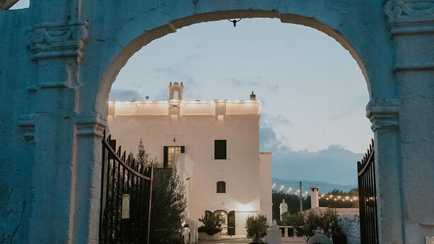 An arched entrance to a building with a stone pathway leading to a gated driveway. - Masseria Mammella with pool and by the beaches (Puglia)