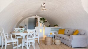 A cozy, white-themed interior with a dining area, a sofa, and a kitchen visible through an arched ceiling. - Masseria Mammella with pool and by the beaches (Puglia)