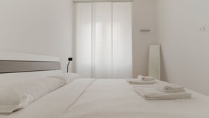 Ein modernes Hotelzimmer mit einem großen Bett, einem Nachttisch, einem Spiegel und einem Fenster mit durchsichtigen Vorhängen.