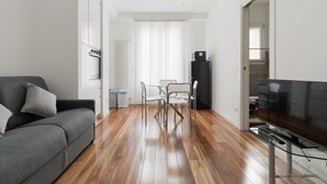 Ein modernes Wohnzimmer mit einer Couch, einem Esstisch mit Stühlen, einem Fernseher und einer Küchenzeile mit Geräten.