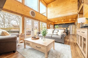 A spacious cabin interior with a wooden ceiling, large windows, a cozy seating area, and a kitchen. - *Stylish 5BD Lodge w/ VIEWS! | Hot Tub + POOL* (Sevierville)