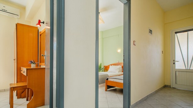 Ein Zimmer mit einem Bett, einem Schreibtisch und einem Stuhl. Eine Tür führt in einen weiteren Raum.