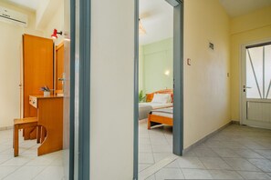 A room with a bed, a desk, and a chair. There is a door leading to another room. - Solena Studios Kavos (Corfu)