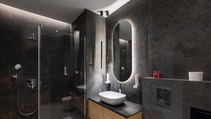 Un baño moderno con ducha de vidrio, un espejo ovalado grande y un tocador de madera.