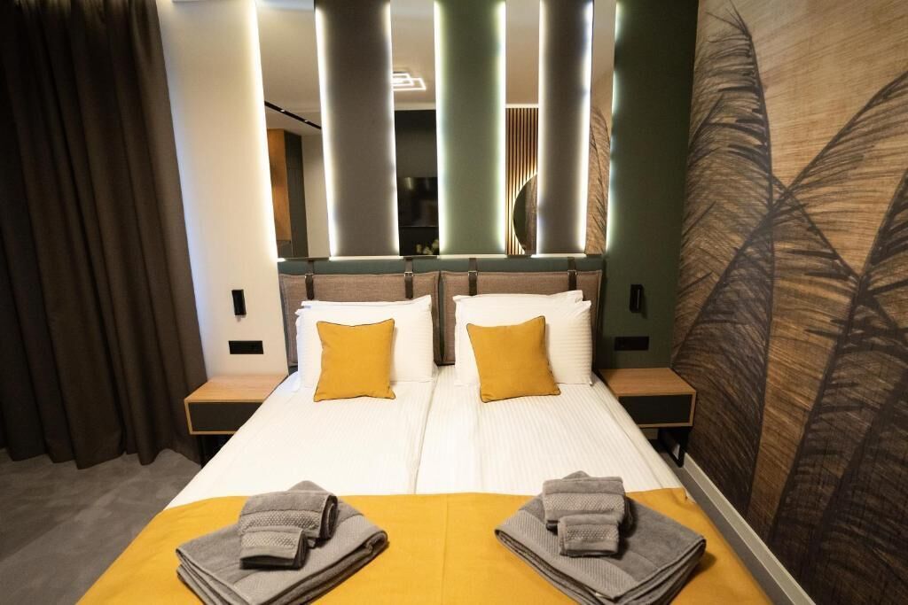 A double bed with two pillows, a bedside table, and a large mirror with vertical light panels.